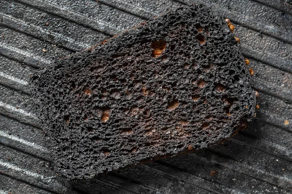 Burnt toast bread slice on a black cast-iron grill pan,, close up. Pattern of burnt black bread, abstract background, macro. Top view