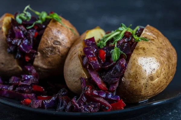 Stuffed potato with red cabbage, tomato, peppers and greens in black plate. Close up