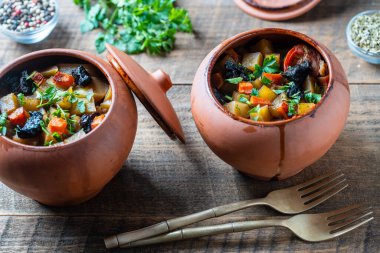 Haşlanmış patates, havuç, soğan, domates ve kuru erik, ahşap kapaklı çamur kaplarda, kapat.