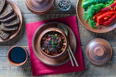 Stewed potato, carrot, onion, tomato and prunes in a clay pots with lid on wooden table background, close up, top view