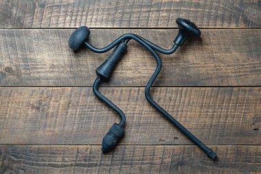 Two crossed black old hand drill on wooden background, top view, close up