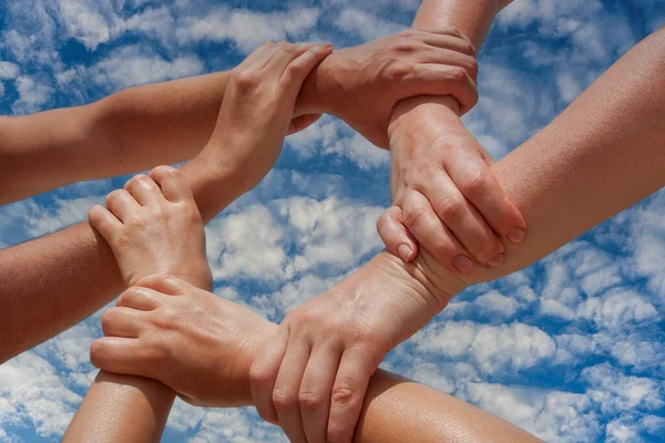 Many hands of people connect or link together community of cooperation on blue sky background, close up. Team support concept