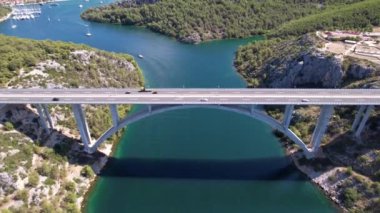 Hırvatistan, Orta Avrupa 'da yaz güneşli bir günde Krka nehri, otostrada ve kemer köprüsünün üzerinde uçmak, seyahat ve doğa kavramı. Güzel manzara ve büyük köprüsü olan mavi deniz. Havadan panorama görünümü