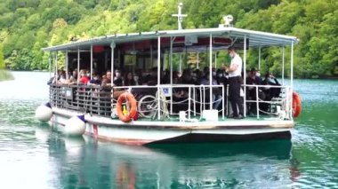 Plitvice Gölleri, Hırvatistan - 30 Ağustos 2021: İnsanlar yaz aylarında Hırvatistan, Orta Avrupa, seyahat ve doğa kavramları ile Plitvice Gölleri kıyıları boyunca turistik bir tekneye biniyor