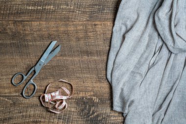 Antique tailor scissors, textile and a tape measure on wooden background, top view, close up
