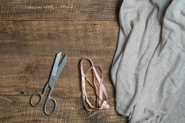 Antique tailor scissors, textile and a tape measure on wooden background, top view, close up
