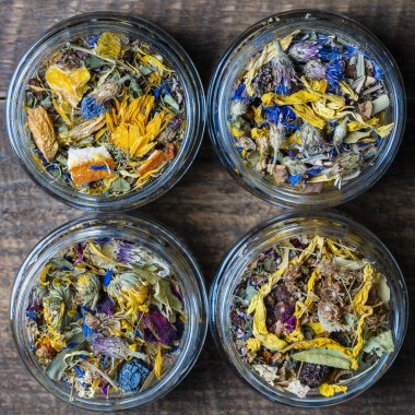 Dry flower and herbal tea leaves in a glass jar on wooden background, copy space. Herbal collection of chamomile, cornflower, mint, sea buckthorn, lemongrass, wild rose, dried citrus fruits and apple