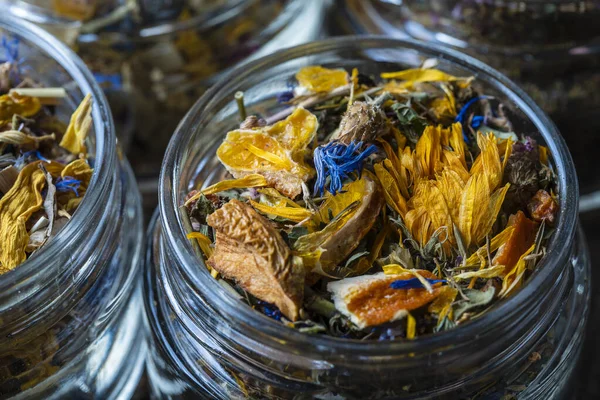 Dry flower and herbal tea leaves in a glass jar on wooden background, copy space. Herbal collection of chamomile, cornflower, mint, sea buckthorn, lemongrass, wild rose, dried citrus fruits and apple