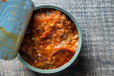 Open canned sardines in tomato sauce on a wooden background, close up, top view