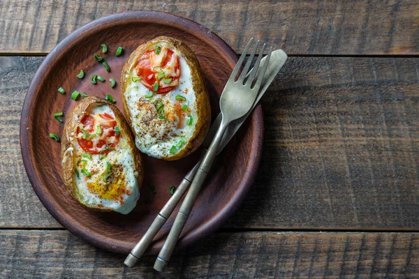 木製の背景にセラミックプレートにチーズ トマト ネギと卵を詰め焼きジャガイモ トップビュー クローズアップ — ストック写真