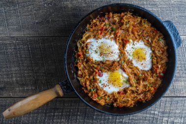 Stewed cabbage with vegetables and fried eggs in a frying pan on a wooden background, close up, top view. Food background. Healthy food
