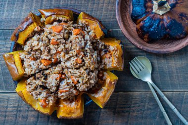 Dolgu malzemesiyle pişirilmiş harika bir balkabağı. Doldurulmuş portakal kabağı, tam pişmiş pirinç, kuru üzüm ve baharat karışımı ahşap masa, üst manzara.
