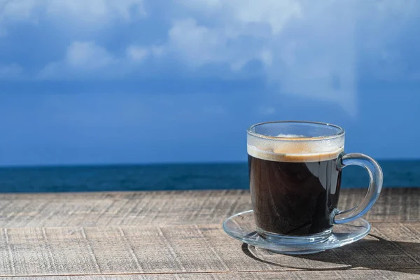 Szklany Kubek Gorącej Czarnej Kawy Drewnianym Stole Morzem Błękitnym Tle — Zdjęcie stockowe