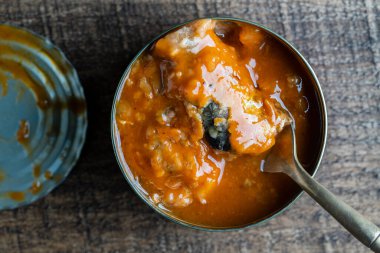 Open canned sardines in tomato sauce on a wooden background, close up, top view