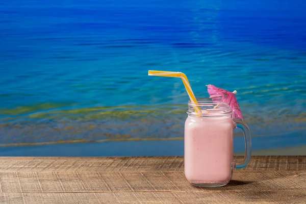 晴れた夏の日に海の水の背景と木製のテーブルの上のガラスマグカップで健康的な冷たいイチゴスムージー コピースペース — ストック写真