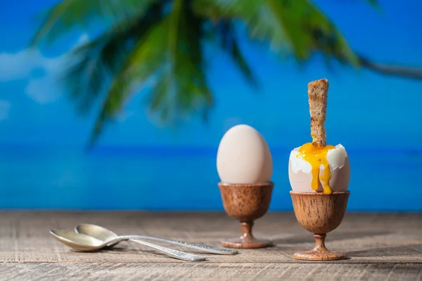 夏日阳光明媚的热带海滨咖啡店 在木制桌子上放上一片烤吐司 配上海水 椰子树和蓝天背景的软鸡蛋 — 图库照片