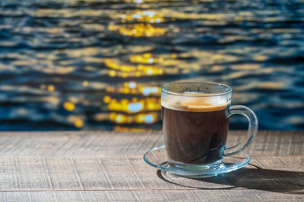 Szklana Filiżanka Gorącej Czarnej Kawy Drewnianym Stole Morskim Tłem Wody — Zdjęcie stockowe