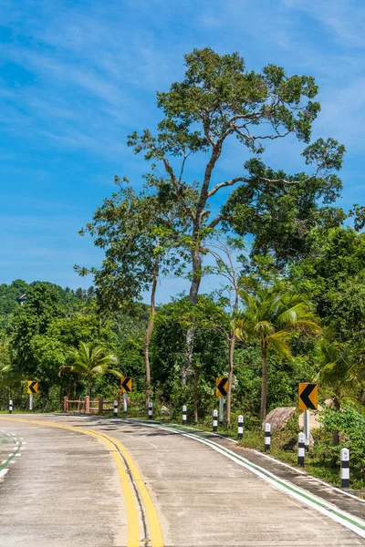熱帯の島 タイの晴れた夏の日に熱帯雨林を通過するターンと標識と空のコンクリート道路 ジャングルを抜ける道 — ストック写真