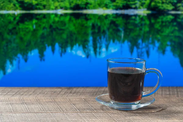 Szklany Kubek Gorącej Czarnej Kawy Drewnianym Stole Tłem Jeziora Lasu — Zdjęcie stockowe