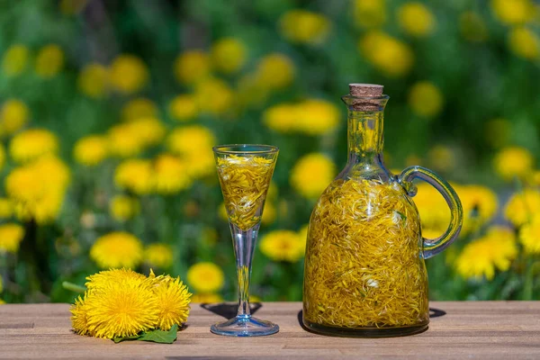 夏の庭の木のテーブルの上のガラス瓶の中に自家製タンポポの花の色合いを閉じます — ストック写真