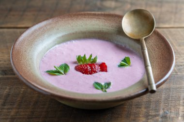 Tahta masadaki seramik kasede yeşil nane yaprağıyla tatlı soğuk çilek çorbası.