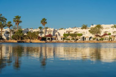 Gündoğumunda, Mısır 'ın Sharm El Sheikh tatil beldesindeki sakin deniz suyuna binalar, güneşlikler ve şemsiyeler yansıtılır.