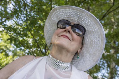 Doğanın arka planında hasır şapkalı, 65-70 yaşlarında mutlu yaşlı bir kadının portresi.