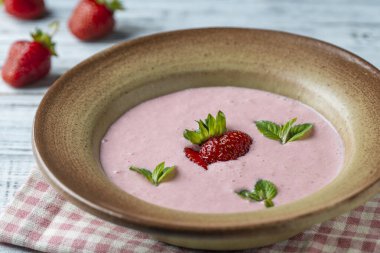 Tahta masadaki seramik kasede yeşil nane yaprağıyla tatlı soğuk çilek çorbası.