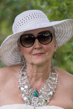 Doğanın arka planında hasır şapkalı, 65-70 yaşlarında mutlu yaşlı bir kadının portresi.