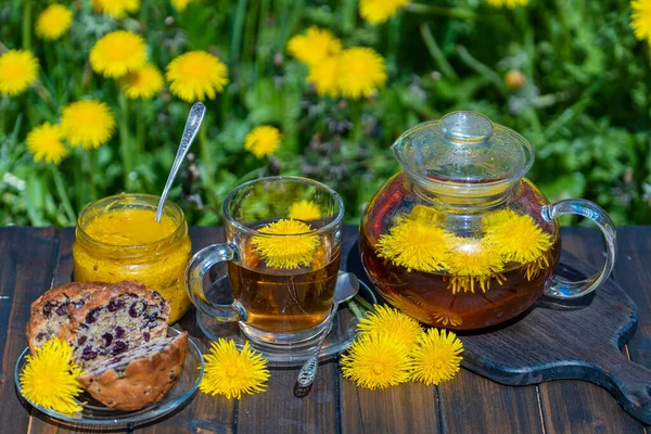 春の庭の木のテーブルの上のガラスのティーポットで健康なタンポポの花のお茶を閉じます — ストック写真