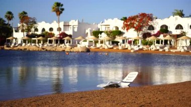 Binalar, güneş panelleri, şemsiyeler ve palmiye ağaçları, Mısır, Afrika 'daki Sharm El Sheikh tatil beldesinde sabahleyin sahildeki sakin Kızıl deniz suyuna yansıyor. Karantina sırasında boş plajlar