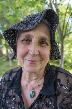 Doğanın arka planında hasır şapkalı, 65-70 yaşlarında mutlu yaşlı bir kadının portresi.