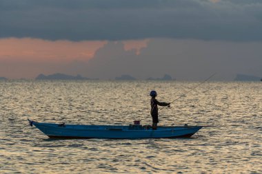 Koh Phangan, Tayland - 21 Şubat 2022: Tayland 'da Koh Phangan Adası' nda gün batımında deniz kenarında bir teknede Tayland balıkçısının silueti