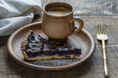 Bir parça yabanmersinli turta ve seramik tabakta bir fincan kahve. Tahta masada nefis bir sabah kahvaltısı.