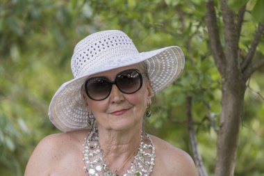 Doğanın arka planında hasır şapkalı, 65-70 yaşlarında mutlu yaşlı bir kadının portresi.