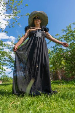 Mutlu yaşlı kadın 65-70 yaşlarında hasır şapkalı, yaz bahçesinde dinleniyor.