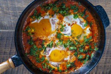 Yumurtalı, domatesli ve maydanozlu nefis shakshuka dökme demir bir tavada, yakın çekim, üst manzara. Shakshuka - Yumurtalı geleneksel İsrail domates yahnisi