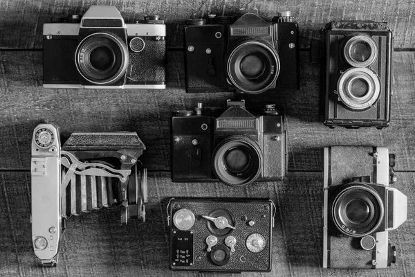 Set of vintage film camera from the times of the USSR on a wooden background, close up, top view. Black and white. Line of old retro cameras
