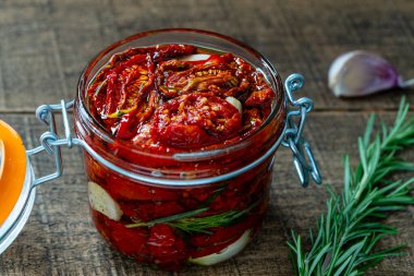 Sarımsaklı, yeşil biberiyeli, güneşte kurutulmuş kırmızı domatesler, ahşap bir masada cam kavanozda zeytinyağı ve baharatlar. Kırsal stil, yakın çekim