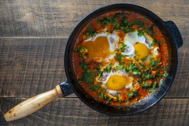 Yumurtalı, domatesli ve maydanozlu nefis shakshuka dökme demir bir tavada, yakın çekim, üst manzara. Shakshuka - Yumurtalı geleneksel İsrail domates yahnisi