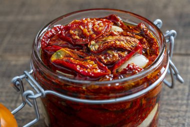 Sarımsaklı, yeşil biberiyeli, güneşte kurutulmuş kırmızı domatesler, ahşap bir masada cam kavanozda zeytinyağı ve baharatlar. Kırsal stil, yakın çekim