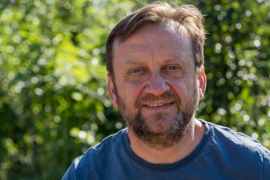 Dışarıda kameraya bakan mutlu olgun bir adamın portresi. Güneşli bir yaz gününde, doğada güler yüzlü, traşsız bir yetişkin adam. İnsanlar ve yaşam tarzı kavramı