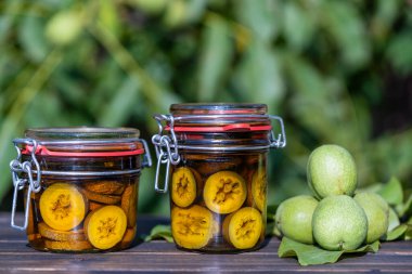 Yaz bahçesindeki ahşap bir masada cam kavanozlarda yeşil ceviz tentürü. Kavanozda alkolle dilimlenmemiş ceviz, ev yapımı tentür hazırlamak için, kapat.