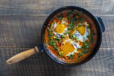 Yumurtalı, domatesli ve maydanozlu nefis shakshuka dökme demir bir tavada, yakın çekim, üst manzara. Shakshuka - Yumurtalı geleneksel İsrail domates yahnisi