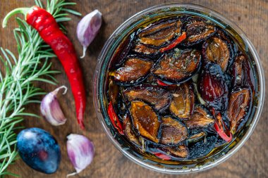 Sarımsaklı güneşte kurutulmuş erikler, yeşil biberiye, kırmızı biber, zeytinyağı ve baharatlar ahşap bir masada cam bir kavanozda. Kırsal stil, üst görünüm, kapat