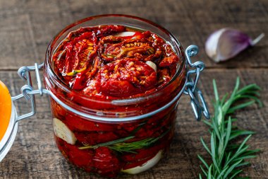 Sarımsaklı, yeşil biberiyeli, güneşte kurutulmuş kırmızı domatesler, ahşap bir masada cam kavanozda zeytinyağı ve baharatlar. Kırsal stil, yakın çekim