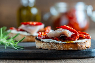 İki dilim ricotta peyniri, bir parça ringa balığı ve ahşap arka planda kurutulmuş kırmızı domates. Lezzetli kahvaltı ya da atıştırmalık şarap. Kapat.