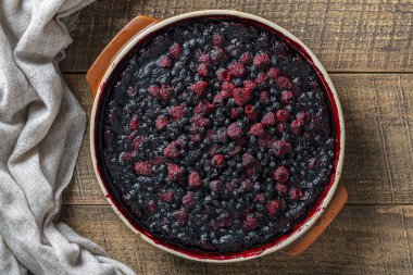 Siyah zemin üzerinde seramik bir tabakta yabanmersinli ve ahudududulu turta.