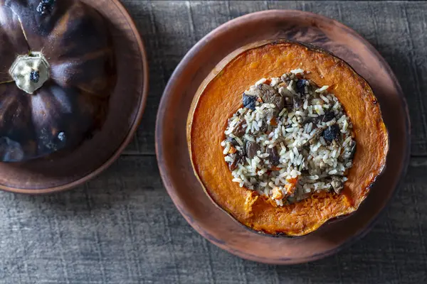 Dolgu malzemesiyle pişirilmiş harika bir balkabağı. Doldurulmuş portakal kabağı, tam pişmiş pirinç, kuru üzüm ve baharat karışımı ahşap masa, üst manzara.