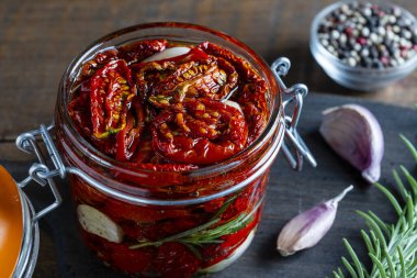 Sarımsaklı, yeşil biberiyeli, güneşte kurutulmuş kırmızı domatesler, ahşap bir masada cam kavanozda zeytinyağı ve baharatlar. Kırsal stil, yakın çekim
